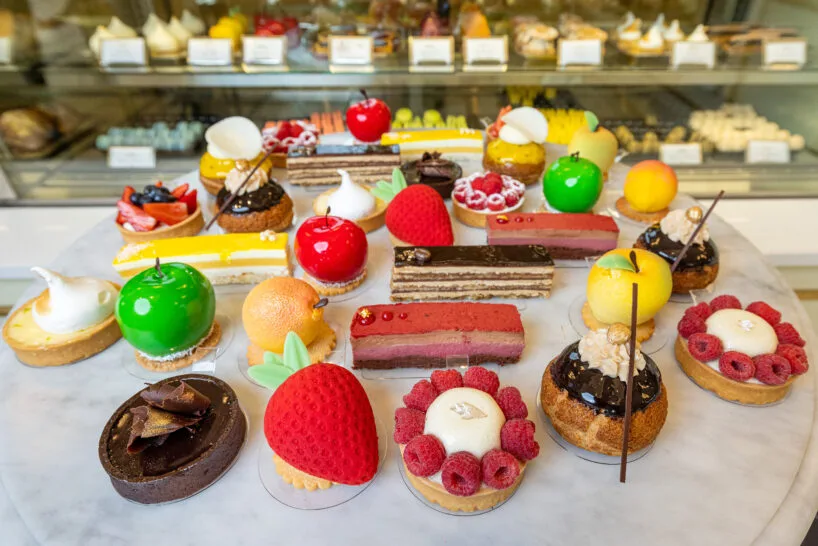 Display of individual pastries at Emma's Patisserie, including tarts shaped like a red apple, a green apple and a strawberry, layered cake slices and raspberry tarts