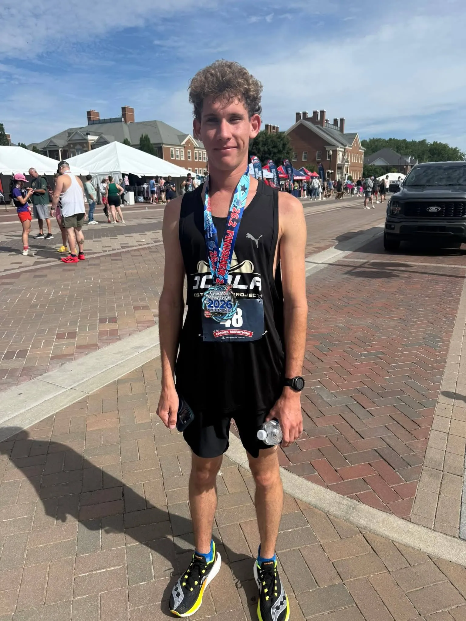 Collin Moore of Ocala at the finish line of the 2026 Carmel Marathon in Indiana, wearing his Ocala Distance Project singlet, bib 48, and finisher medal