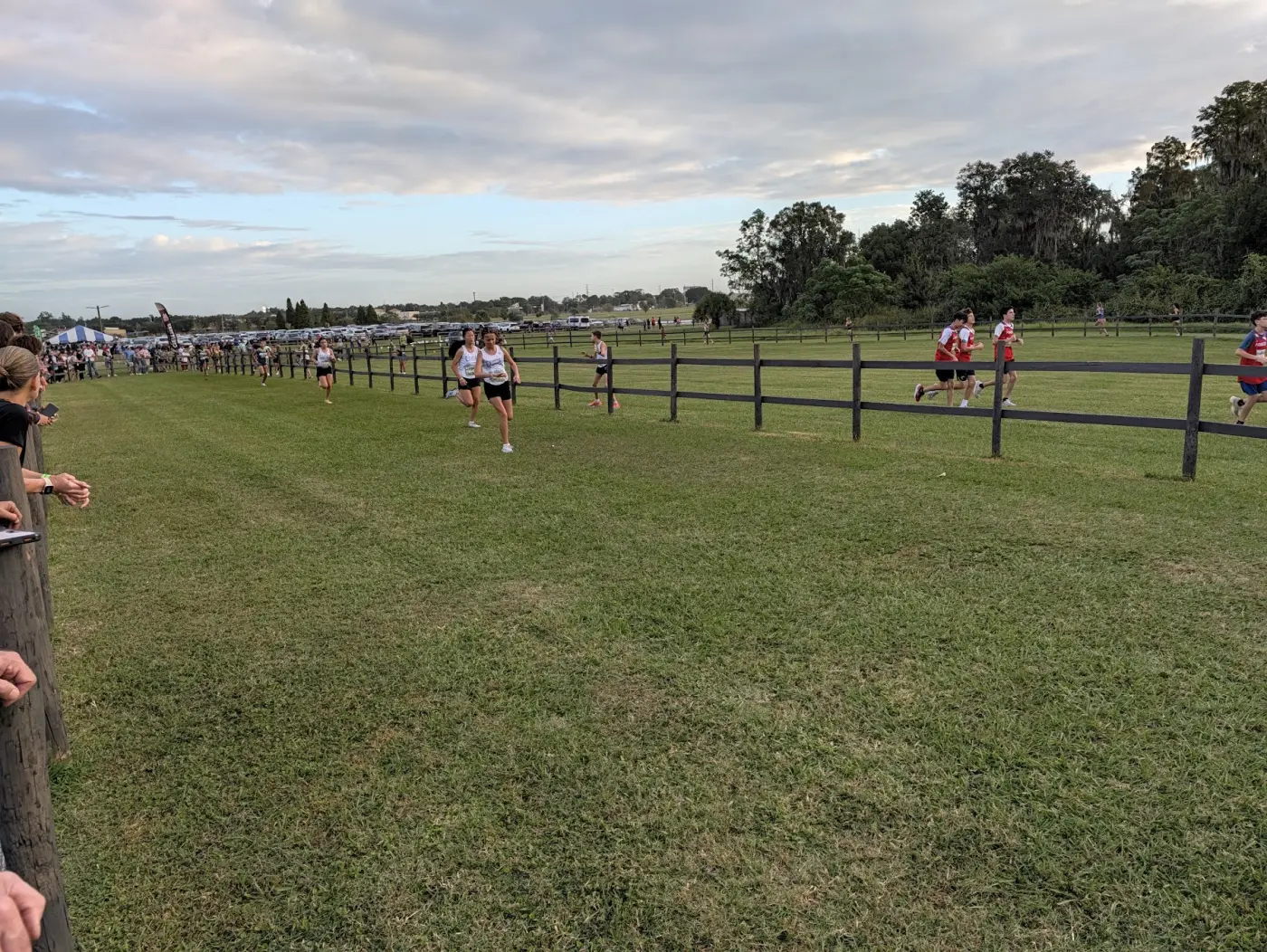 Middle school girls running along a wooden fence line at Holloway Park during the public school girls 3K at the 2026 FLYRA state cross country championships