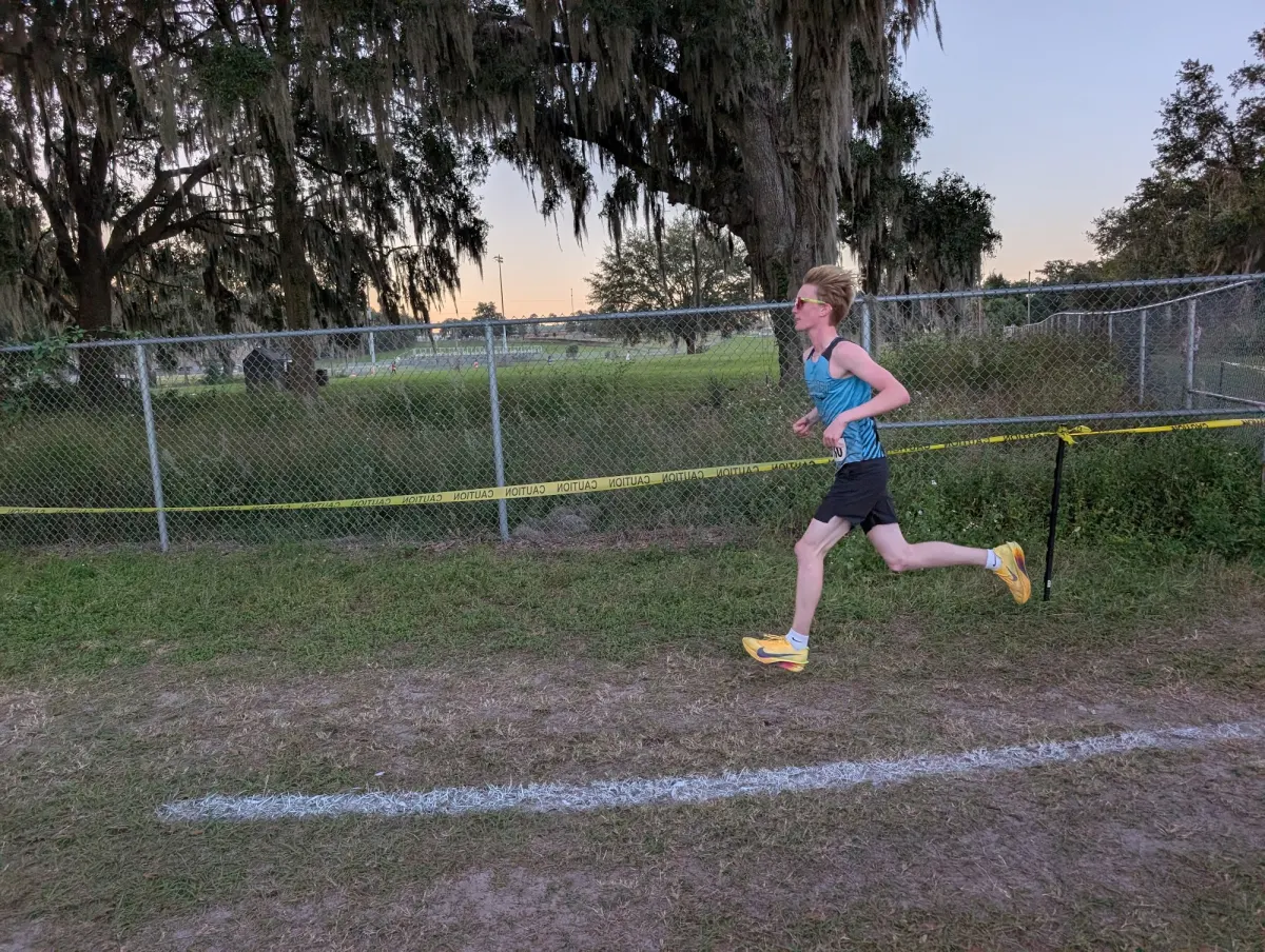 A West Port High School runner in a teal and black singlet on the Belleview High School cross country course during the 2026 Marion Athletic Conference championships