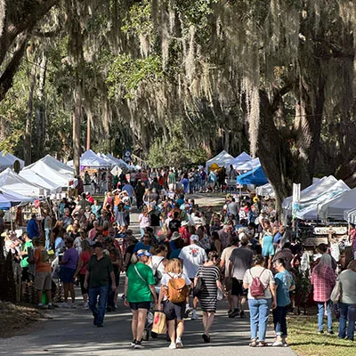 Crowds walking between white vendor tents under moss-draped live oaks at the McIntosh 1890s Festival in McIntosh, Florida