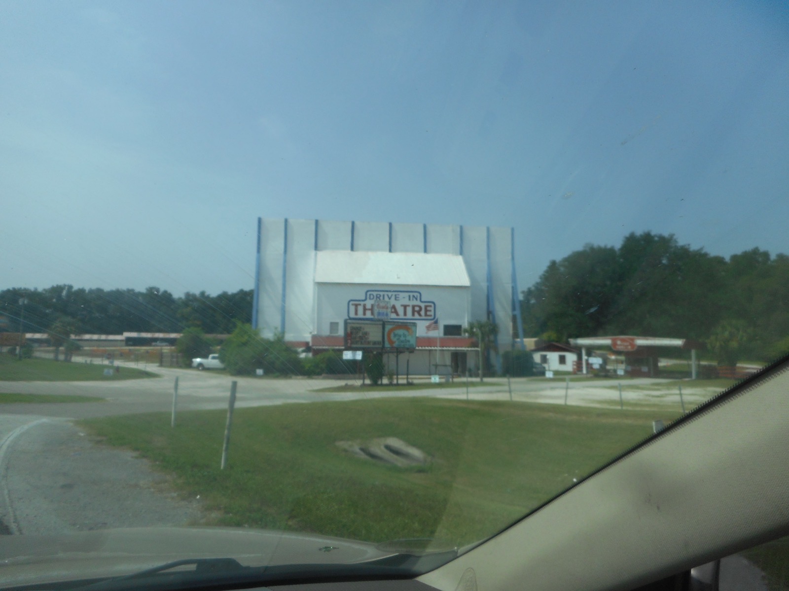 The white Ocala Drive-In screen tower with "Drive-In Theatre" painted on it, seen through a car windshield from the entrance road