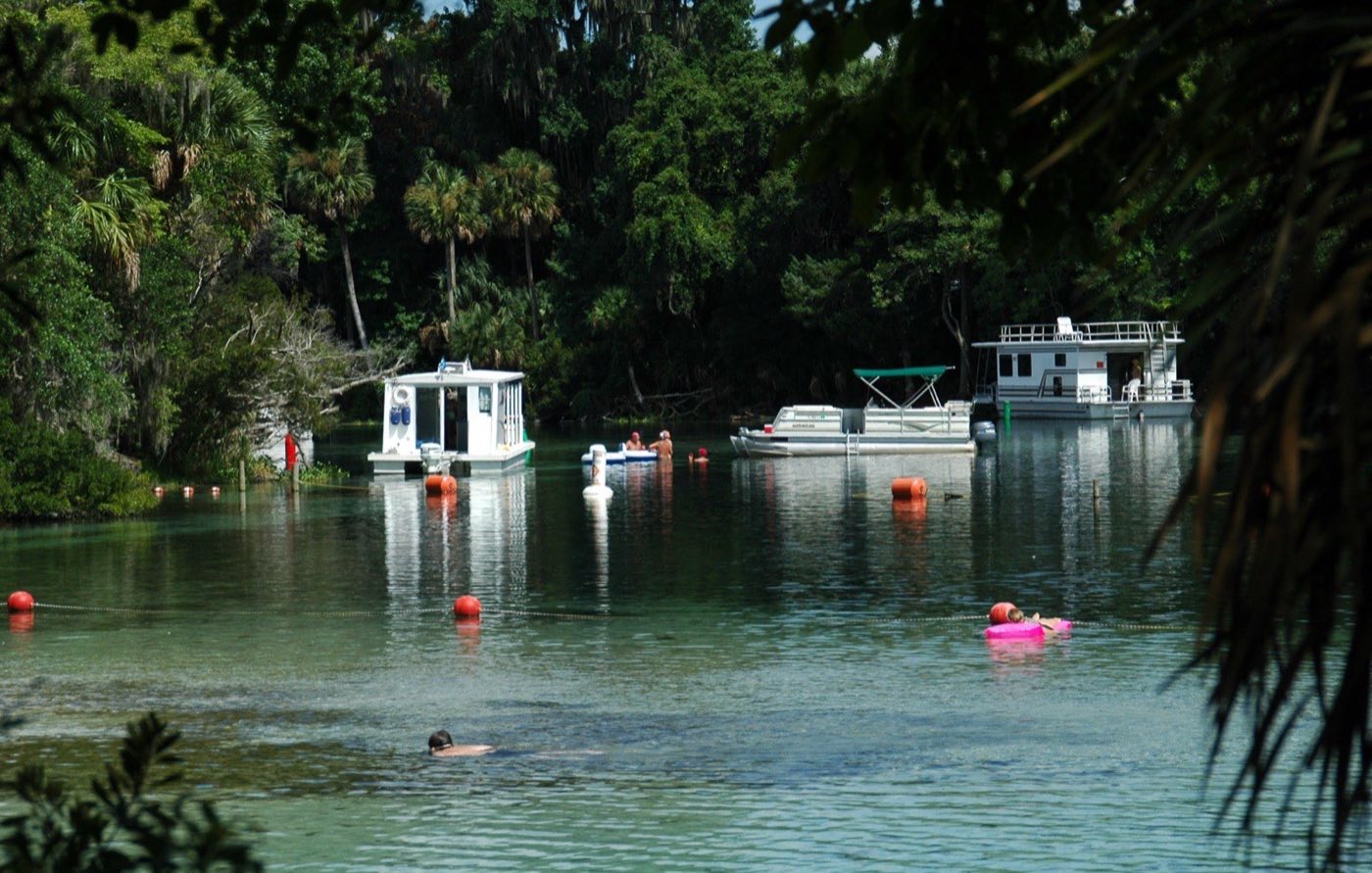 Pontoon boats anchored on the Silver Glen Springs run beyond a line of orange buoys, with a swimmer in the foreground