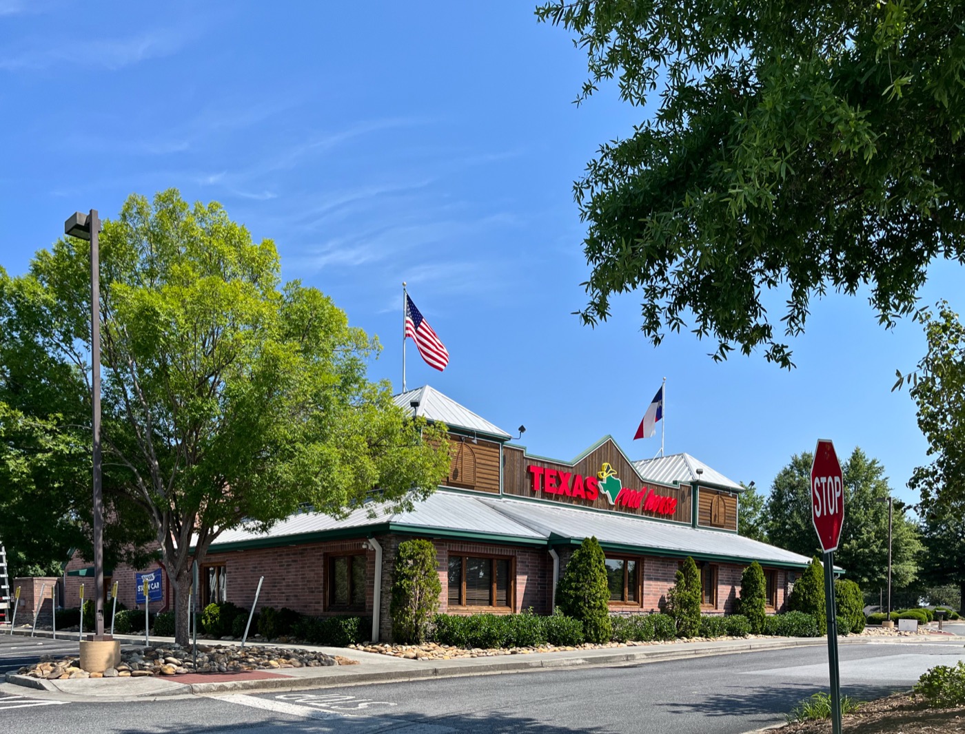 Brick and wood exterior of a Texas Roadhouse restaurant with the red Texas Roadhouse sign and flags on the roof