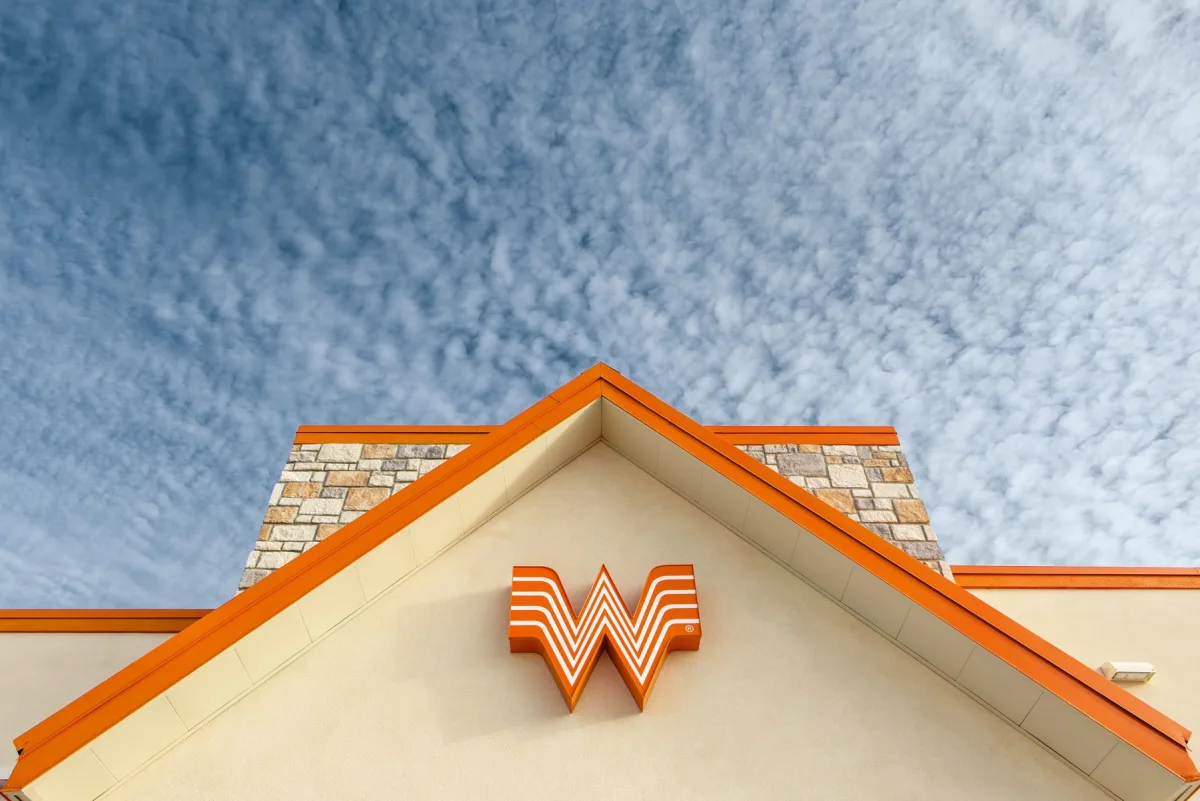 Whataburger's orange Flying W logo on the gable of a restaurant under a blue sky